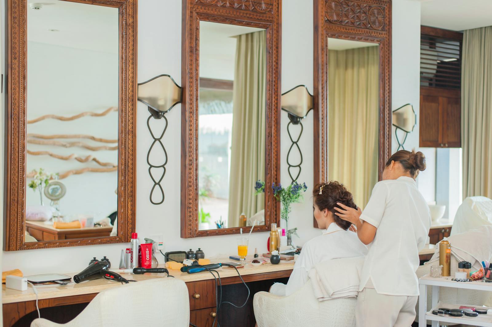 Elegant hair salon interior featuring mirrors, wooden decor, and a hairstylist attending to a client.