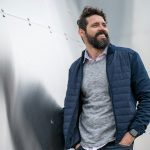 man in blue zip up jacket standing beside white wall