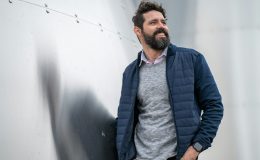 man in blue zip up jacket standing beside white wall
