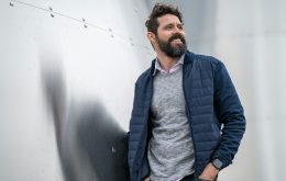 man in blue zip up jacket standing beside white wall